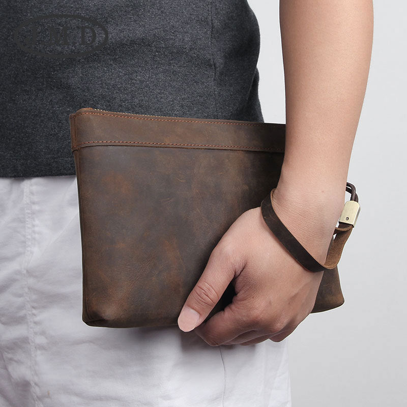 Pochette en cuir marron tenue à la main, avec bracelet en cuir et boucle métallique