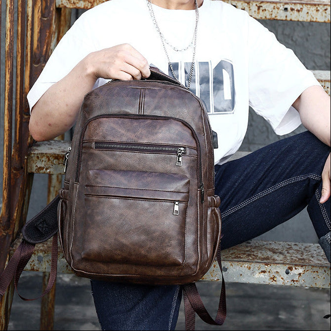 Sac à dos en cuir marron vintage avec poches zippées, porté par une personne en jean et t-shirt blanc